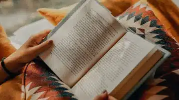 person reading book on brown and beige textile