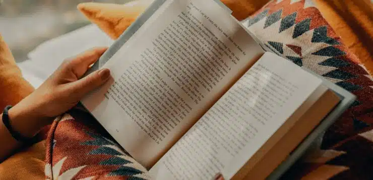 person reading book on brown and beige textile