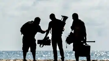 silhouette of men holding camera standing on sand near body of water during daytime